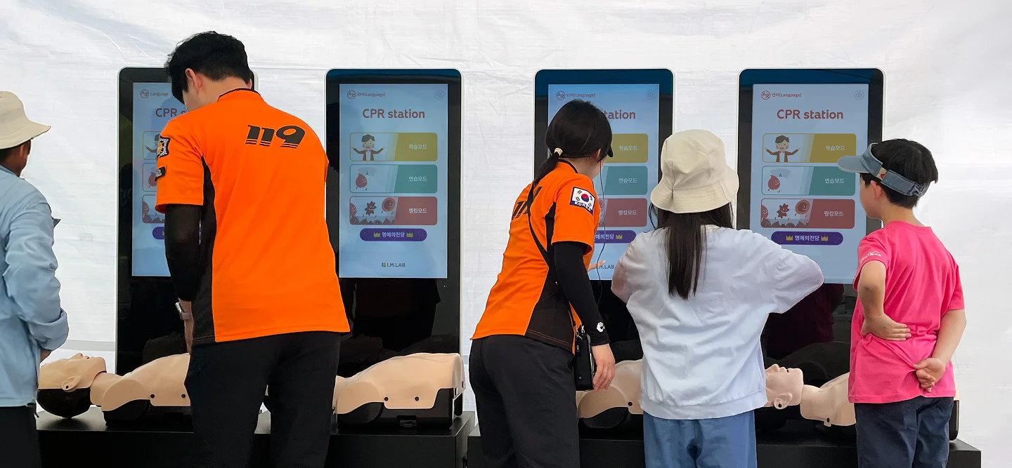 야외 행사장에서 방문객과 구급대원이 CPR station 키오스크 4대로 실습하는 모습